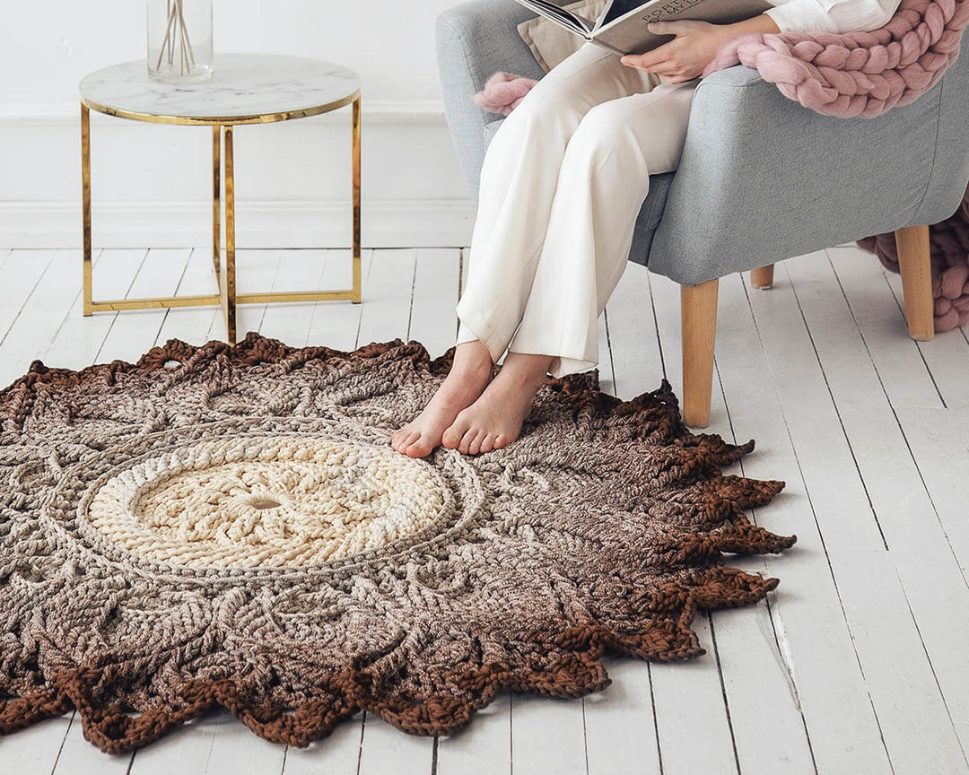 Round crochet rug on a wooden floor with a person sitting on a chair in the background.
