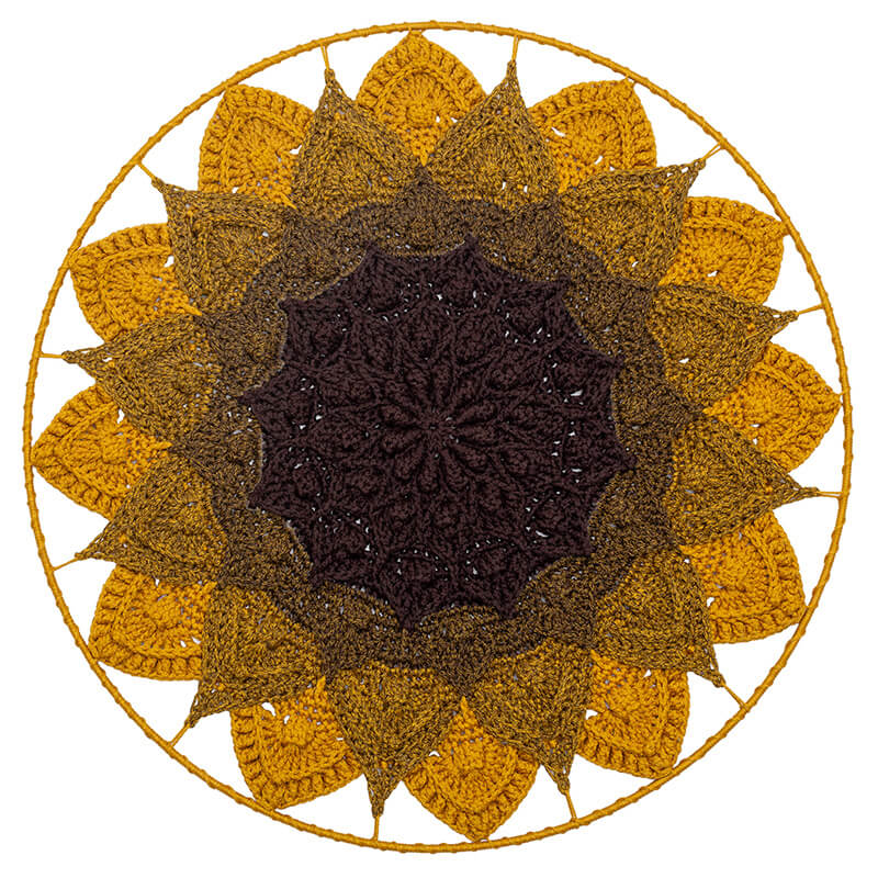 Round crochet wall hanging with sunflower design in brown and yellow on a white background