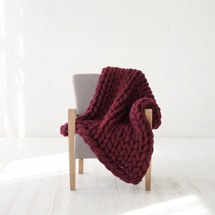 Burgundy Kiss chunky knit merino wool lap blanket draped over the arm of a grey armchair
