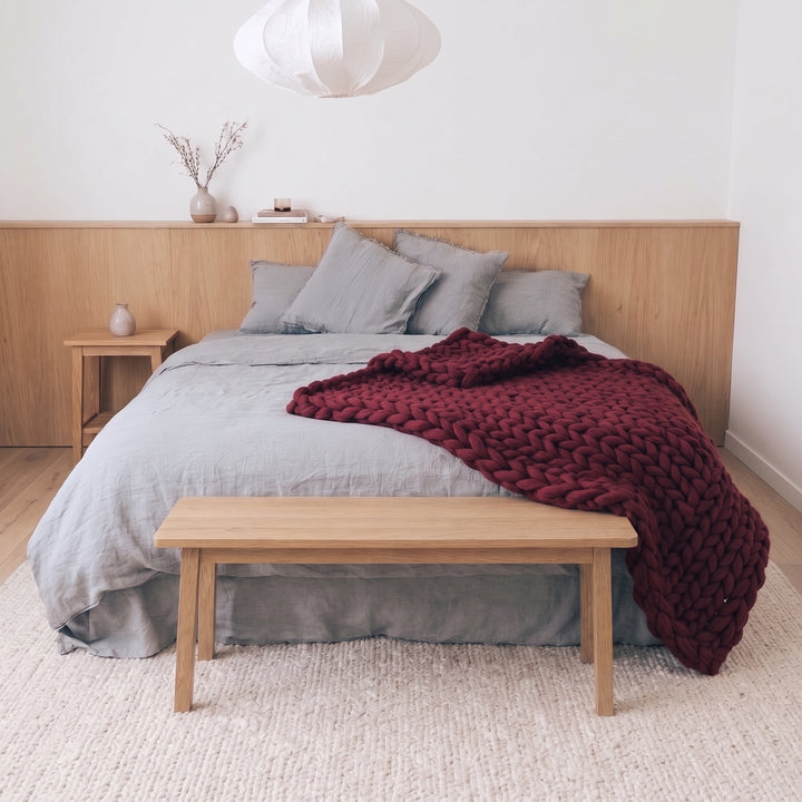 Burgundy Kiss chunky knit merino wool throw blanket on a bed with grey linen bedding