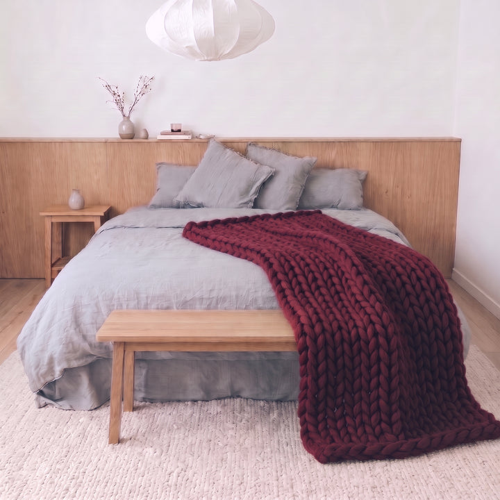 Burgundy Kiss twin size chunky knit merino wool blanket on a bed with grey linen bedding