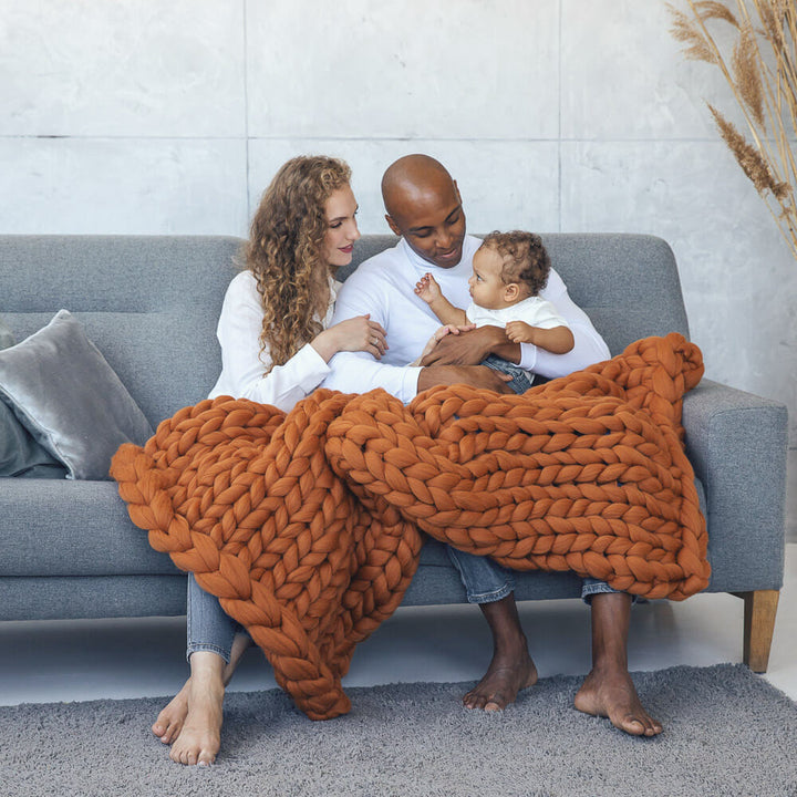 family wrapped in butternut color chunky knit blanket  sitting on the sofa