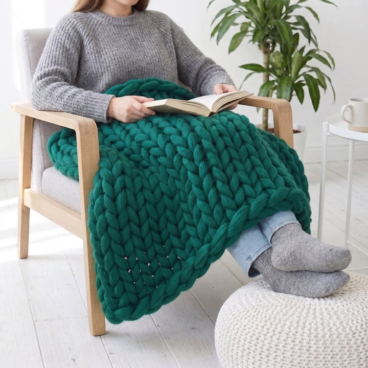 Woman reading in an armchair with an emerald green chunky knit lap blanket over her legs