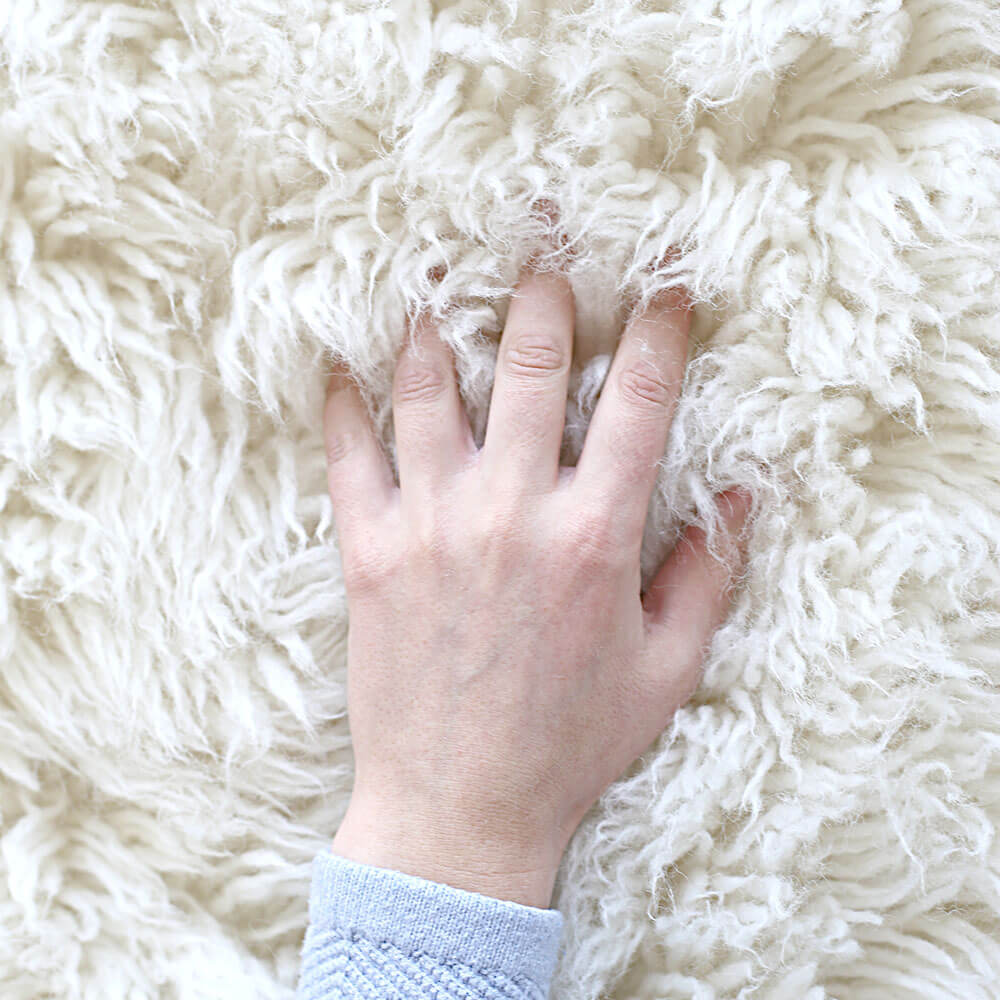 close up hand sticking fingers into fluffy wool flokati rug