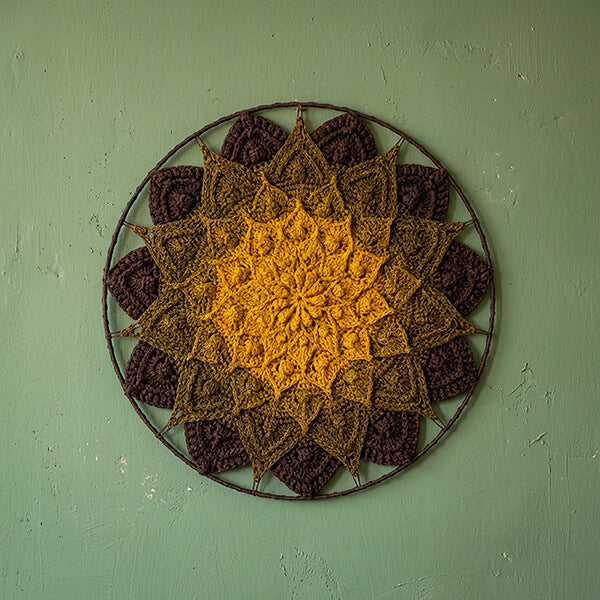 Crocheted wall art with a sunflower design on a green wall