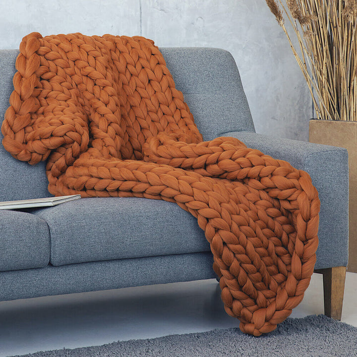 large chunky knit blanket in ginger color draped over the grey sofa