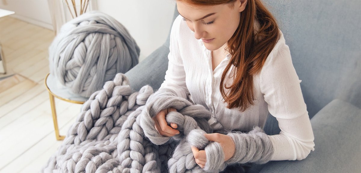 girl sitting on armchair and knitting chunky knit blanket