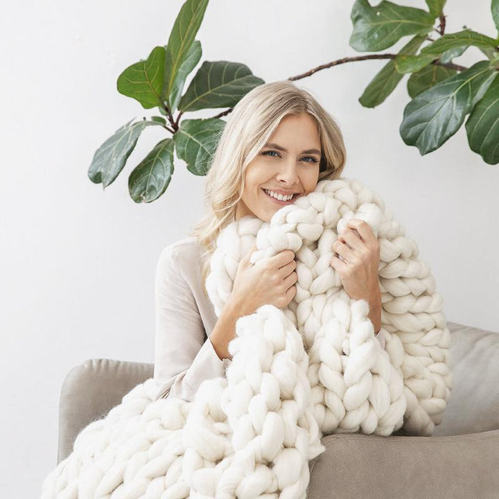 a girl wrapped in white chunky knit blanket on a chair