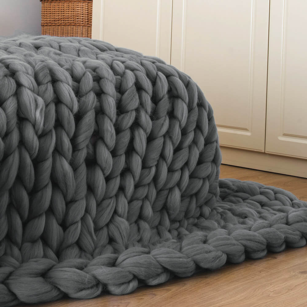 gray bulky knit blanket made of merino wool draped over the corner of the bed