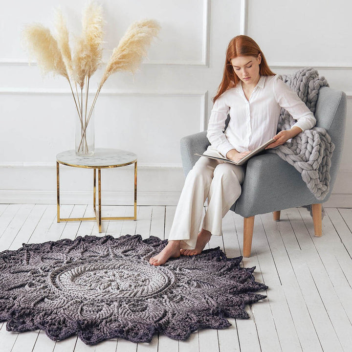 Woman reading a book in a cozy room with a large crochet rug on the floor.