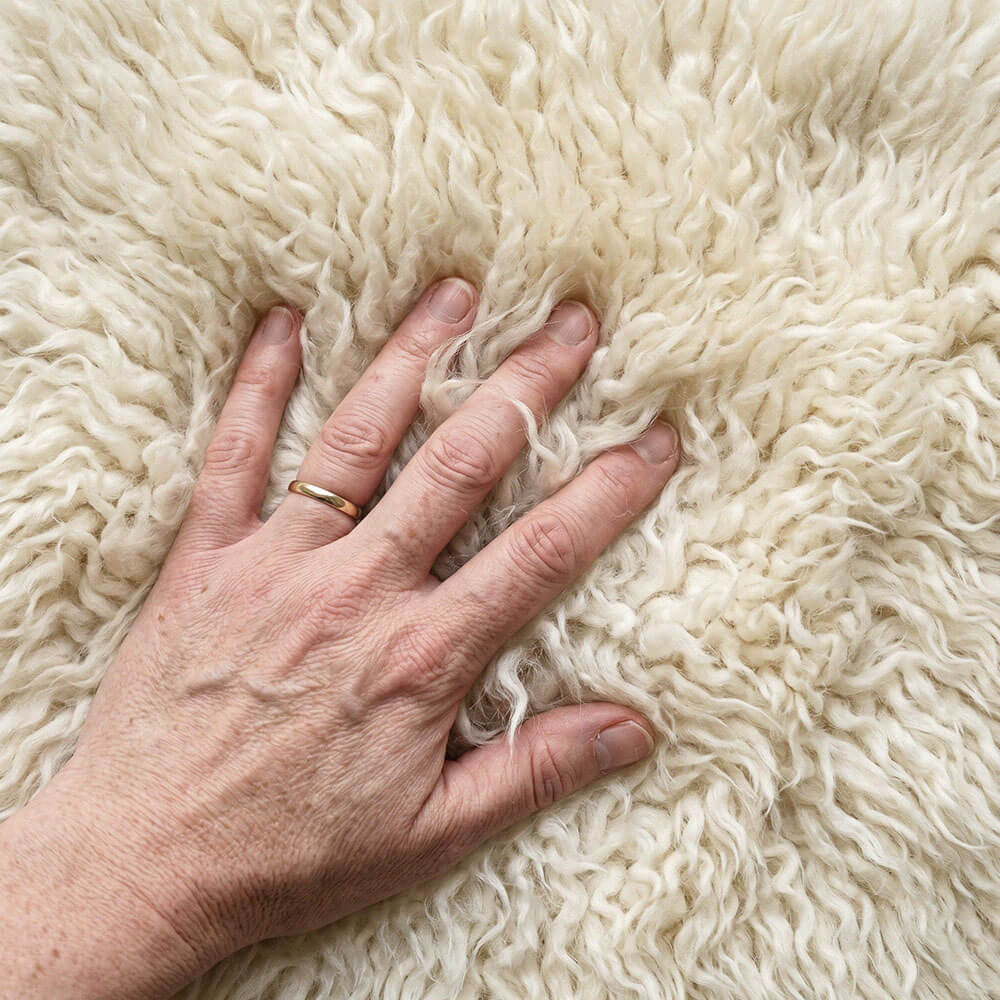 Hand with a gold ring on a fluffy white flokati rug