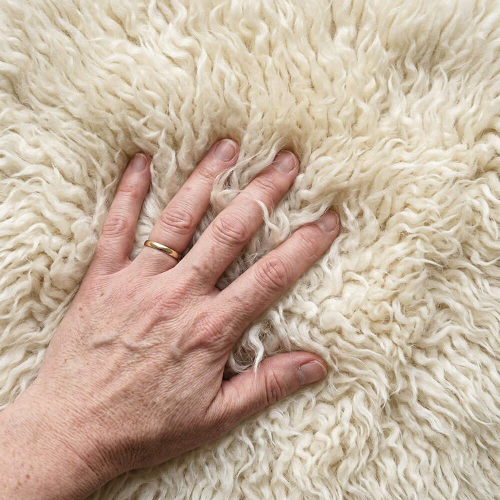 Hand with a gold ring on a fluffy white flokati rug