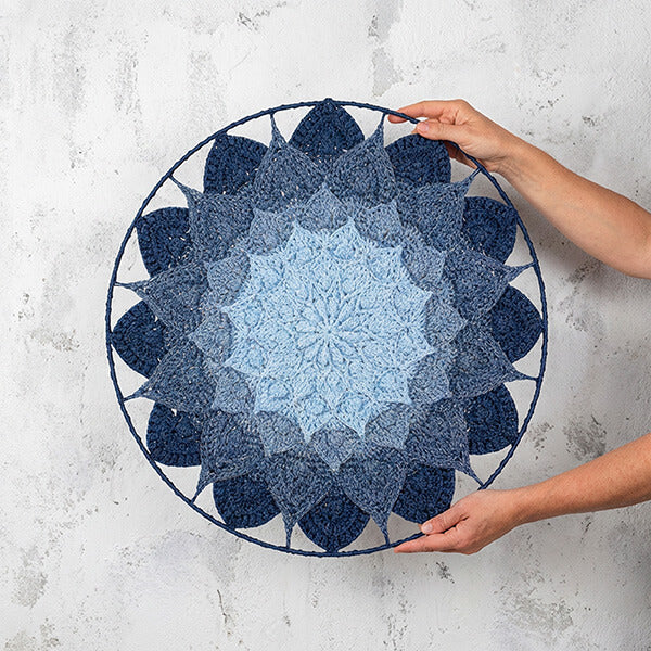 Handmade blue mandala wall art held by a person against a textured white wall.