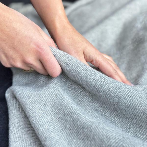 hands lifting grey merino wool blanket close up