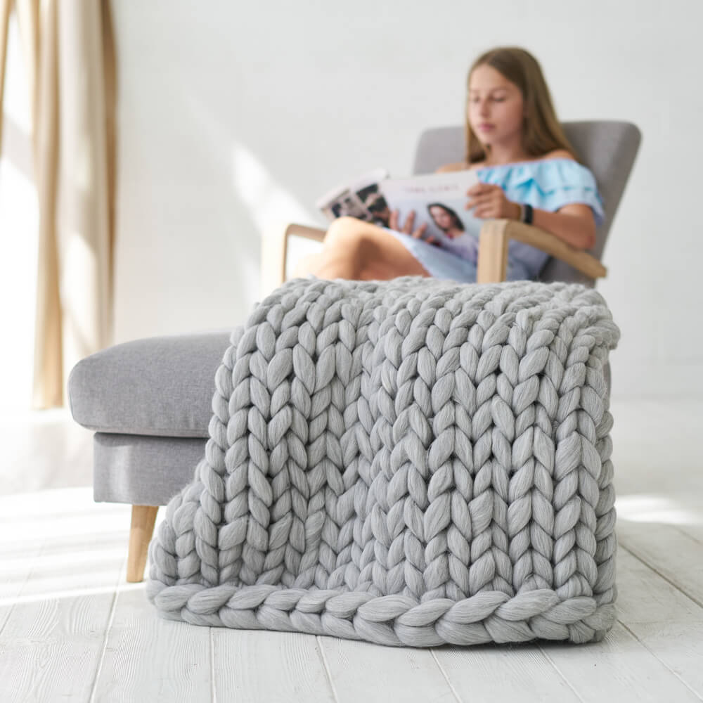 light grey chunky knit throw draped over ottoman and girls sitting on a chair in background