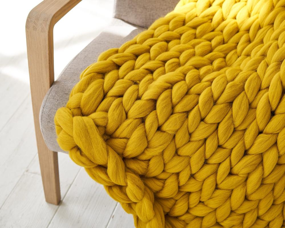 mustard chunky knit blanket on a grey armchair