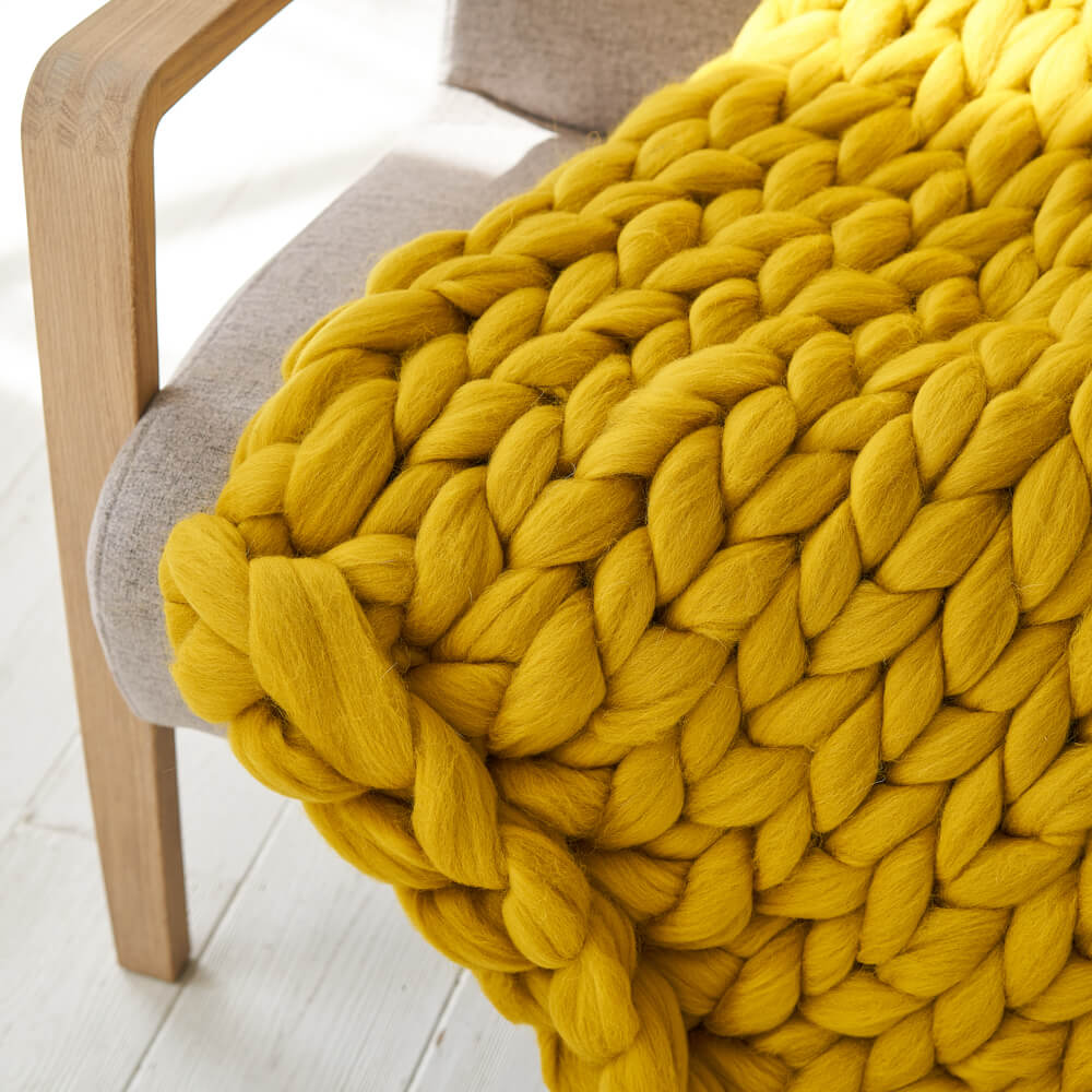 a mustard giant knit blanket on the chair