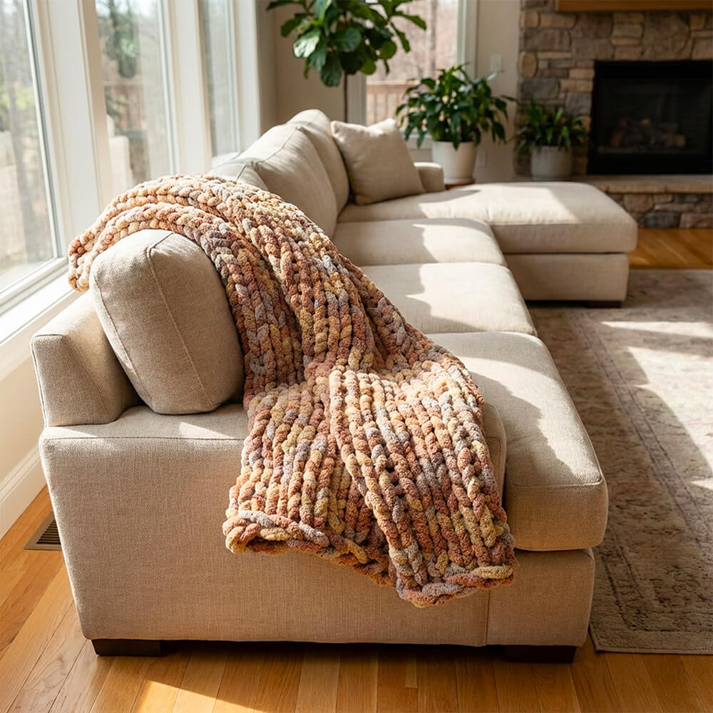 Beige sectional sofa with a chunky chenille knitted blanket in a sunlit living room.