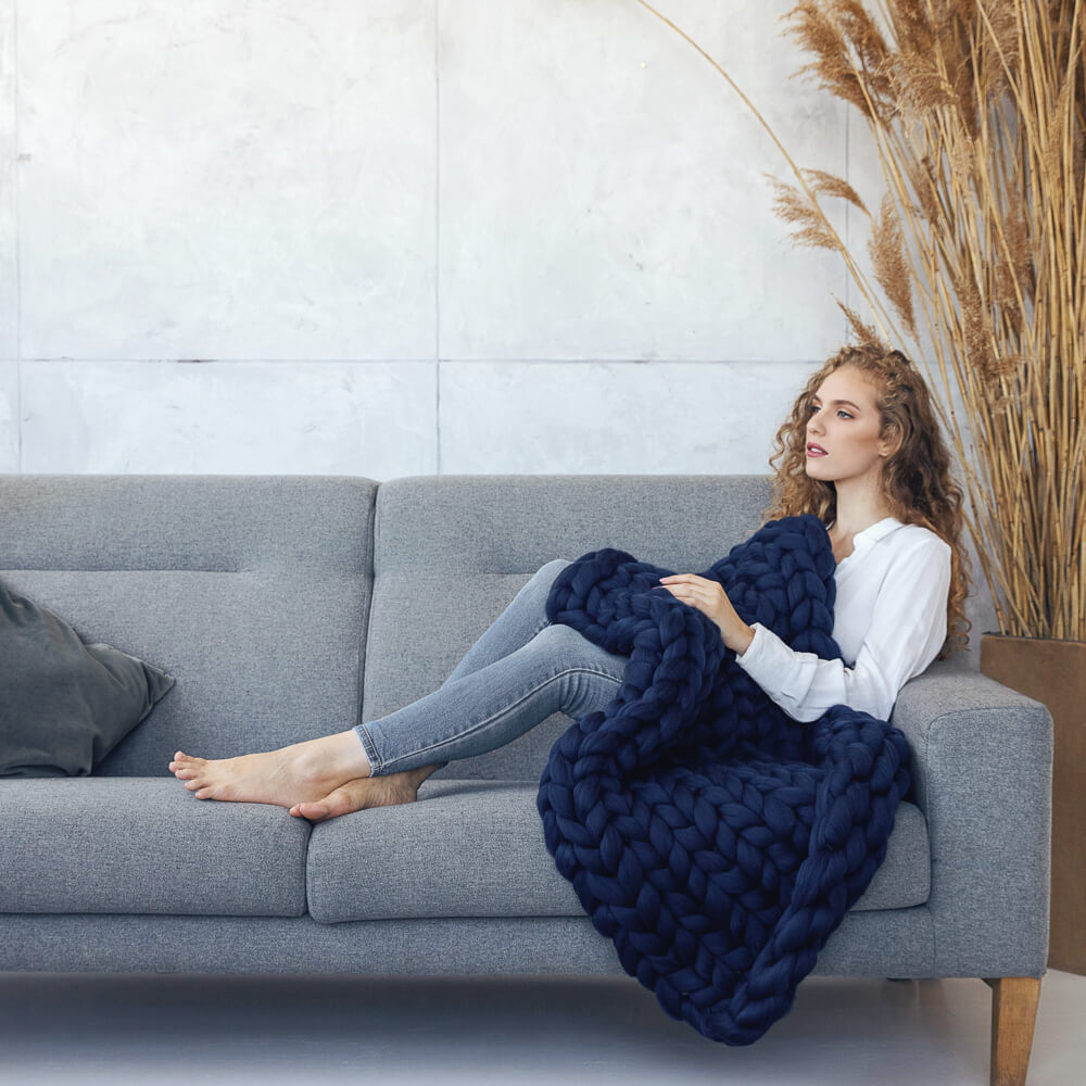 lady sitting on the couch and covered with navy chunky knit blanket