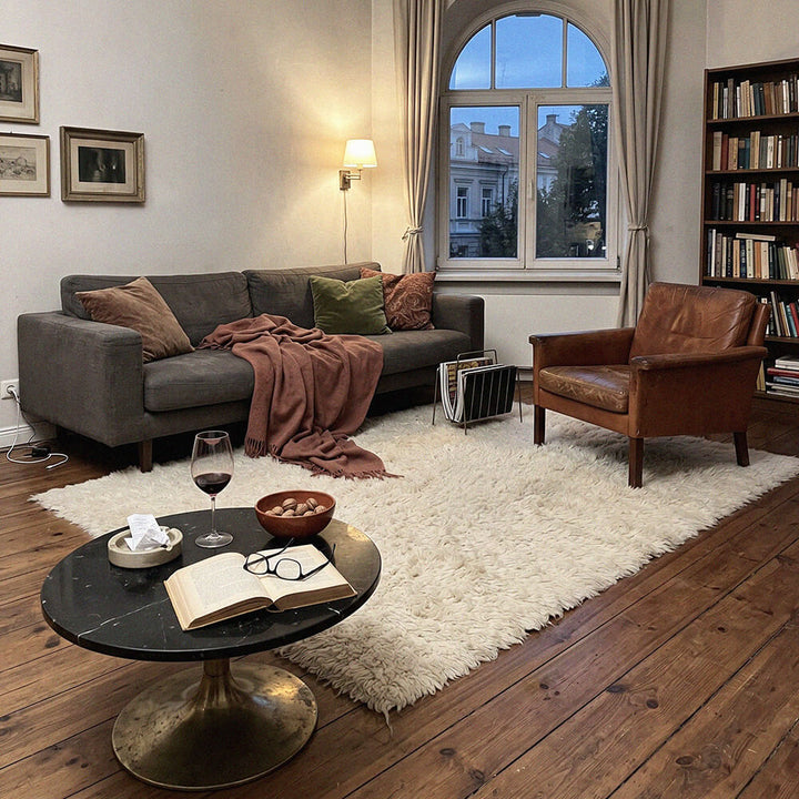 Cozy living room with a gray sofa, brown armchair, and a small round table with a book and wine glass.