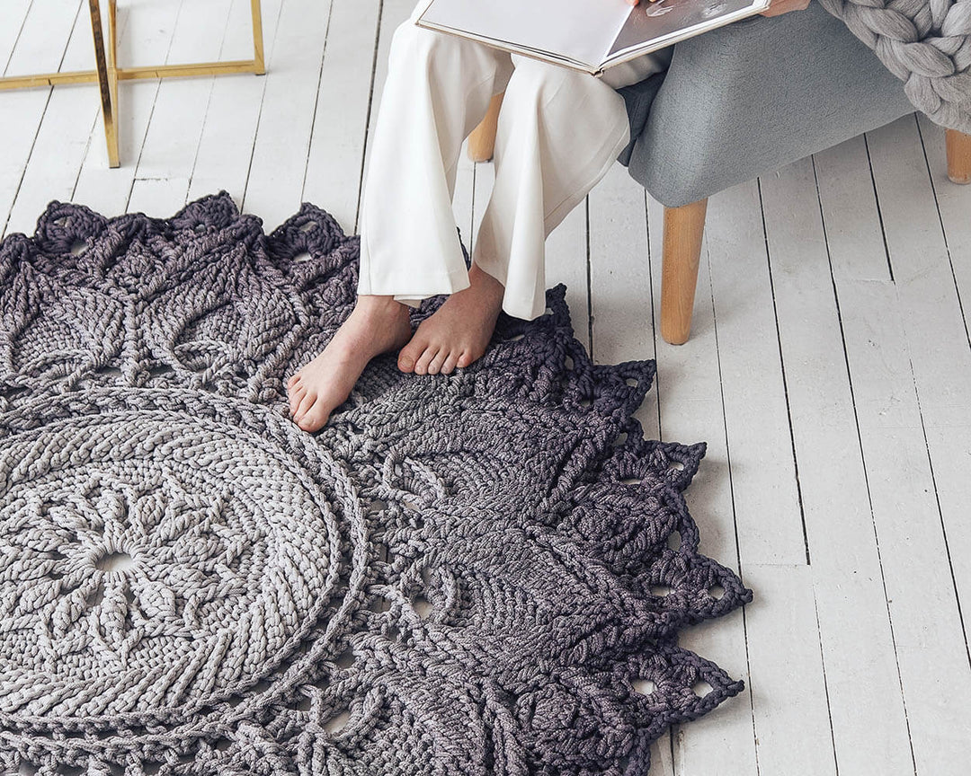 Gray crocheted rug on a wooden floor with a person sitting on it.
