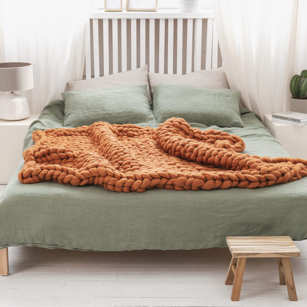 orange chunky knit blanket draped over the bed with light green bedding