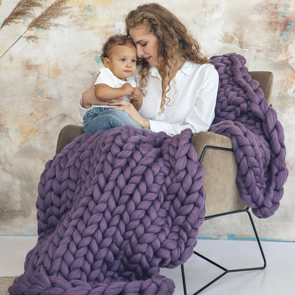 mother and her little buy sitting on the chair wrapped in purple chunky knit blanket