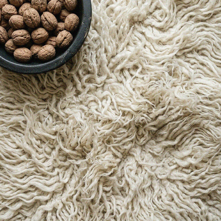 Close-up of a textured beige surface with a bowl of walnuts.
