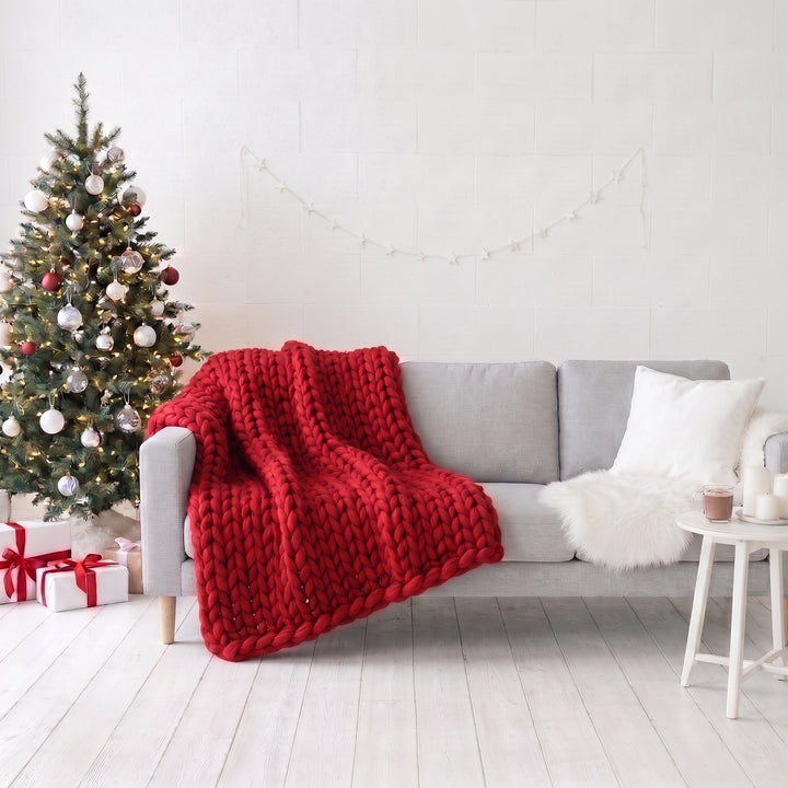 Tulpenrote grob gestrickte Merinowolldecke auf einem hellgrauen Sofa neben einem Weihnachtsbaum in einem weißen Wohnzimmer
