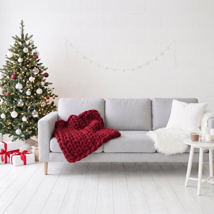 Rote grob gestrickte Decke aus Merinowolle auf einem hellgrauen Sofa neben einem Weihnachtsbaum in einem weißen Wohnzimmer