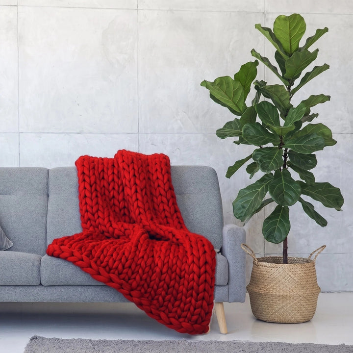 Plaid en grosse maille tricoté main en laine mérinos XXL coloris Tulipe, posé sur un canapé gris