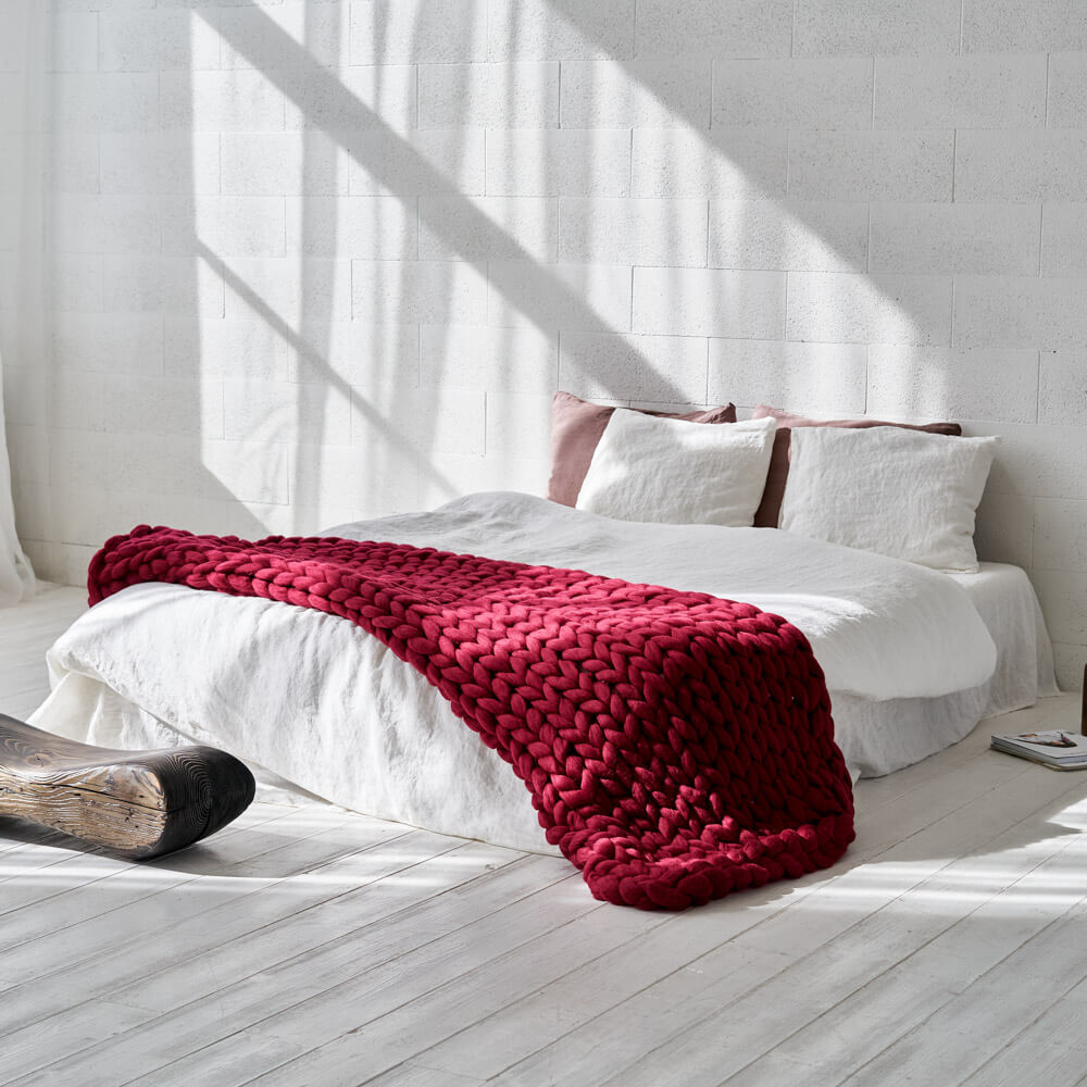 bordo twin xl size chunky knit blanket draped over the bed with white bedding in a white room