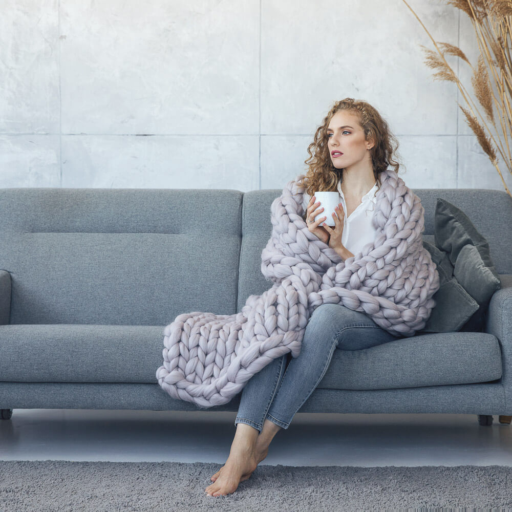 lady wrapped in twin size chunky knit blanket sitting on the sofa and holding a cup of coffee