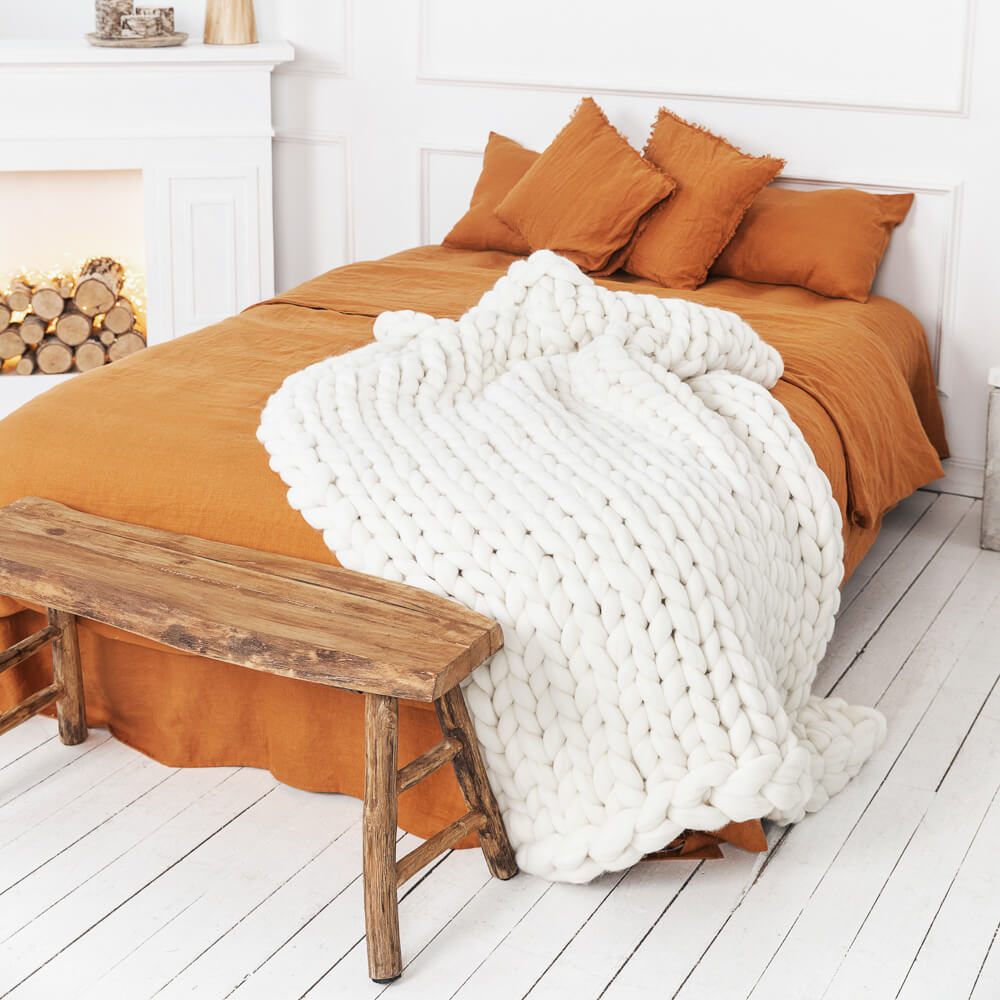 white chunky knit blanket 120X150cm draped over the bed with orange bedding in a cozy white room