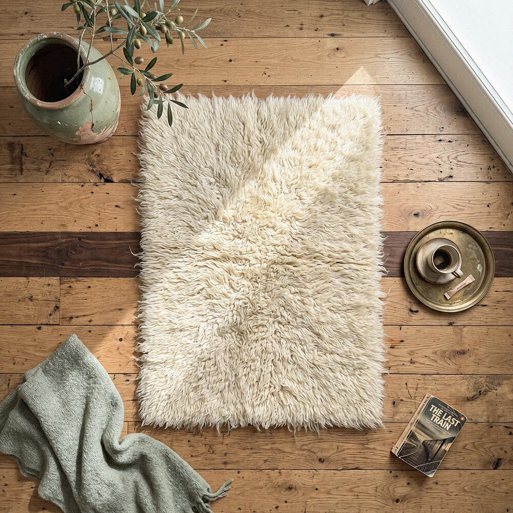 White fluffy rug on a wooden floor with a plant and books nearby