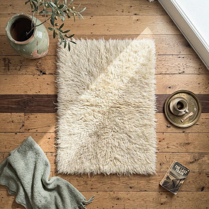 White fluffy rug on a wooden floor with a plant and books nearby