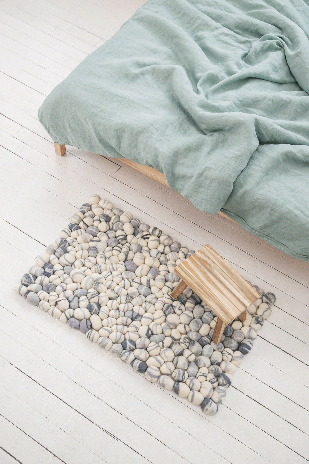 white with grey elements felted wool pebbles rug from the top at the bed with green bedding